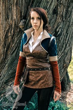 a woman standing in front of a tree wearing a brown and blue outfit with white collar