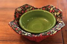 a green bowl sitting on top of a wooden table next to a black and red flower