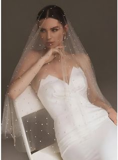 a woman wearing a wedding veil and sitting on a chair with her hand under her chin