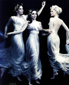 three women in white dresses standing under a veil