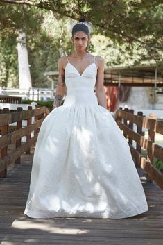 a woman in a white wedding dress standing on a wooden bridge with trees behind her