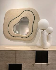 a mirror sitting on top of a dresser next to a white vase and two lamps