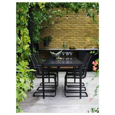 an outdoor dining table with four chairs and two wine glasses on it in front of a brick wall