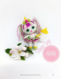 a small doll is sitting next to some flowers on a white background with pink and green trimmings