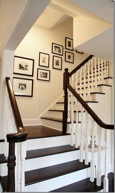 a staircase with framed pictures on the wall and wooden handrails, along with black and white stairs