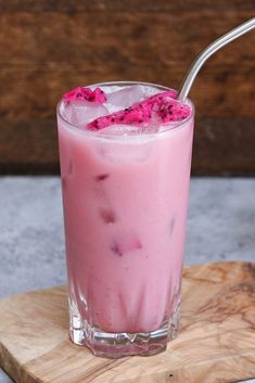 a pink drink in a glass on a wooden tray with a straw sticking out of it