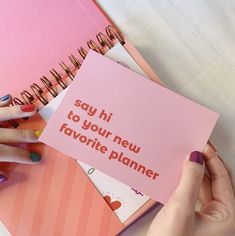 a woman holding a pink notepad with the words say hi to your new favorite planner