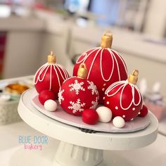 three red and white ornaments are sitting on a cake platter in the shape of christmas baubles