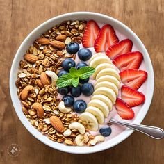 a bowl filled with yogurt, bananas, strawberries and nuts on top of a wooden table