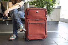 a woman sitting on a bench next to a piece of luggage with her legs crossed