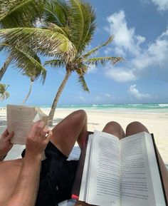 a man reading a book on the beach with a palm tree in the foreground