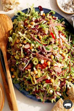 a salad on a blue plate with wooden spoons and other food items around it