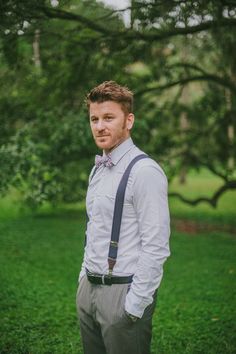 a man wearing a bow tie and suspenders standing in the grass with his hands on his hips