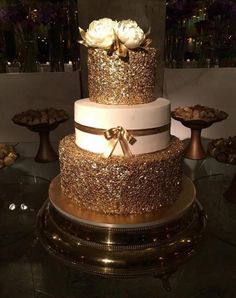 a three tiered cake with gold glitter and white roses on top is displayed for the camera