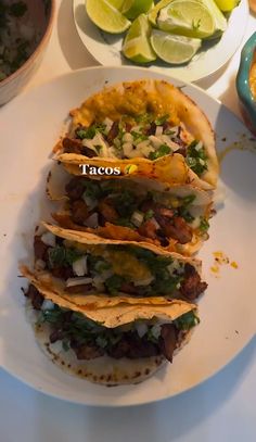 three tacos sitting on top of a white plate next to limes and other food