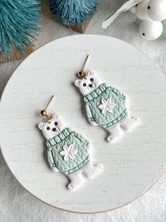 two white cats wearing sweaters are sitting on a plate next to some blue ornaments