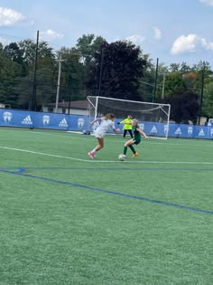 two girls playing soccer on a field with trees in the backgrouds and blue sky