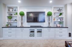 an entertainment center with white cabinets and black counter tops in a living room area that has carpeted flooring and built - in shelving