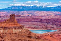 the mountains are covered with snow in the distance, and there is a blue lake surrounded by red rocks