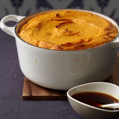 there is a large casserole on the table next to a bowl of sauce