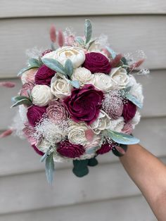 a bridal bouquet with purple and white flowers is being held by someone's hand