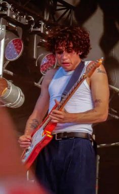 a man holding a guitar in his right hand and looking at the camera while standing on stage