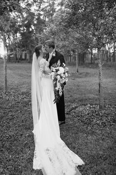 black and white photo of bride and groom kissing in the grass with trees behind them