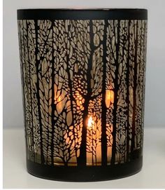 a candle that is sitting in front of a glass vase with trees on it and two candles inside