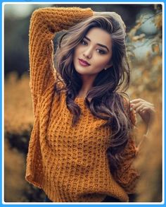 a woman with long hair wearing a yellow sweater posing for a photo in a field