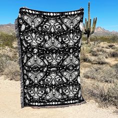 a black and white blanket sitting on top of a dirt field next to a cactus