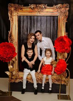 a family posing for a photo in front of a gold frame with red flowers on it