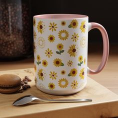 a yellow and pink coffee mug sitting on top of a cutting board next to a spoon