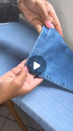 someone is sewing something on top of a blue cloth with one hand and two fingers