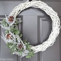 a white wreath with pine cones and greenery