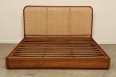 a wooden bed frame with bamboo headboard and foot board on concrete flooring in an empty room