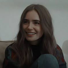 a smiling woman sitting on top of a couch next to a white wall in a living room