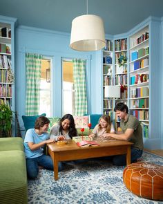 three people sitting at a table in a living room with bookshelves behind them