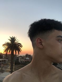 a man with no shirt on standing in front of a palm tree and buildings at sunset