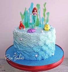 there is a cake with blue frosting and little mermaids on it, along with other decorations