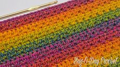 a crocheted rainbow blanket with a knitting needle