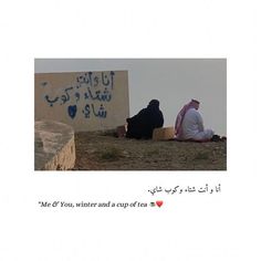 two people sitting on the ground near a wall with graffiti written in arabic and english