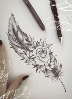 a drawing of a rose and feathers on a sheet of paper next to some pens