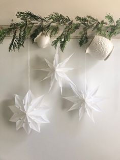 three white paper snowflakes hanging on a wall next to evergreen branches and ornaments