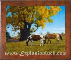 two horses graze in the grass under a tree with yellow leaves on its branches