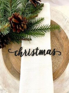 a napkin with the word christmas written on it next to pine cones and evergreen branches