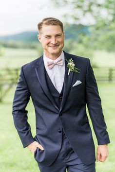 a man in a tuxedo smiles at the camera while standing on some grass