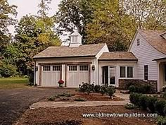 a white house with two garages in the front yard and trees on both sides