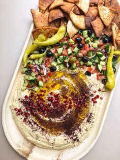 a platter filled with hummus, olives, peppers and pita chips