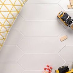 toy cars and construction equipment are on the floor in front of a white tiled wall