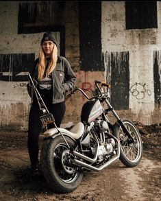 a woman standing next to a motorcycle in front of a building with graffiti on it